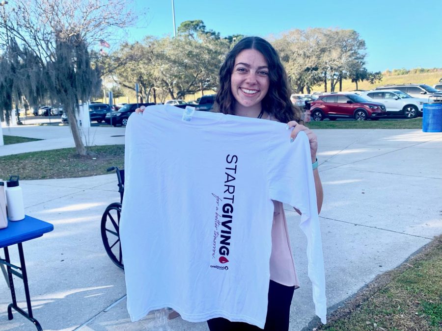 Rachel, a one blood staff member, is seen holding up a free t-shirt they give out to the blood donors.