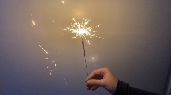 A hand holding a sparkler on New Years Eve with a white background. 