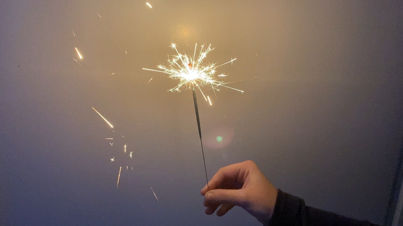 A hand holding a sparkler on New Years Eve with a white background. 